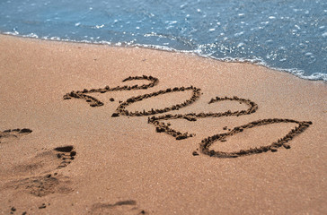 Symbols 2020 written on sand. New Year concept.