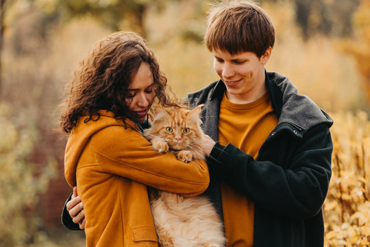 Young couple with a red cat on a background of an autumn park.