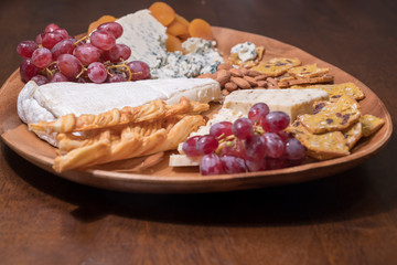 Wooden cheese platter with brie, assorted cheeses, red grapes, crackers and nuts