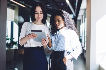 Inspired multiethnic businesswomen surfing tablet in office lobby