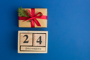 Brown gift boxes with red ribbons and fir tree branch on blue trendy background. Festive backdrop for projects. Flat lay style. Top view. Color of the year. Christmas Eve Date On Calendar. December 24