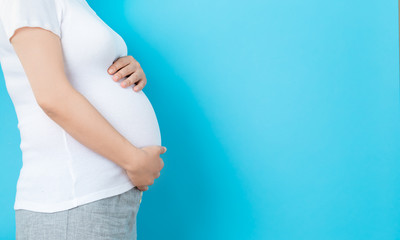 Pregnant woman on a solid background holding her belly