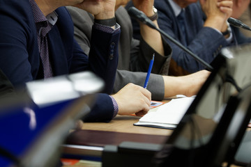 Participants in a business meeting with notebooks, pens, watches, and monitors carefully listen to the speaker. Work time. Business style. Close-up - obrazy, fototapety, plakaty