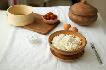 Cooking breakfast of salted cottage cheese with jam. The rustic style is complemented by ceramic dishes, a wooden cutting board and a sieve.