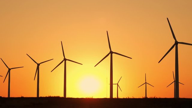 Motion the blades of a large wind turbine in a field against a background of orange sunset on the horizon with a bright disk sun. Alternative energy sources. Windy park. Ecological energy.Industrial 