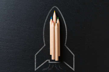 Drawing of a rocket on a black metal background with pencils. Startup concept