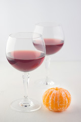  two glasses with red wine and peeled mandarin on an old wooden white countertop