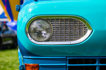 Turquoise blue old classic antique American car half front, left side, close up and selective focus on glass headlight with metallic chrome frame