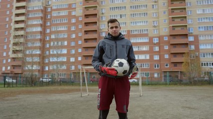 Zoom in shot of professional middle eastern goalkeeper in sportswear and gloves playing with soccer ball and looking at camera with confidence while posing on outdoor playing field