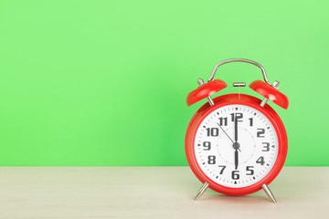 Red retro alarm clock with six o'clock, on wooden table on a green background. The concept of time, holiday, event start, deadline. Layout with copy space for your text.