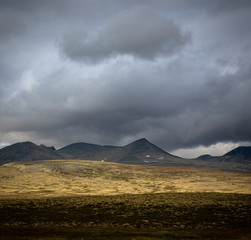 Autumn in Rondane National Park, mountain range and dark, cloudy sky, Norway.