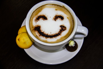 the cup of coffee with smile on the table. The biscuits with candy. Smile. Be happy with coffe