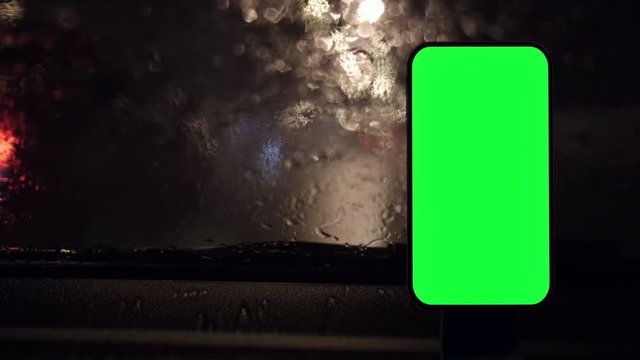 Green screen smartphone at car dashboard. Night rainy highway at background. For navigation, taxi or car sharing app.