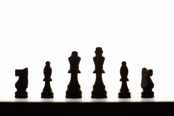 Chess pieces on a board. Backlit with a white background.