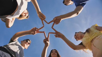 Friends make a star shape from their hands against a blue sky
