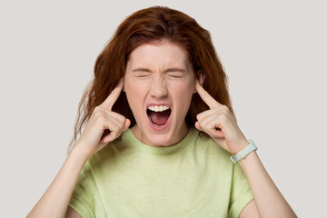 Head shot portrait young woman sticking plugging fingers in ears.
