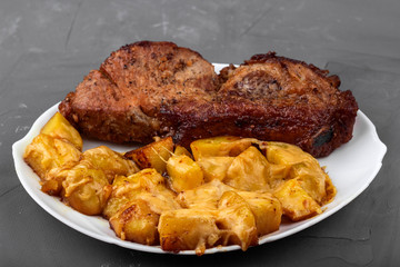 Pork loin steak and potatoes baked with cheese on a white plate
