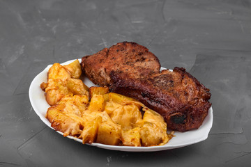 Pork loin steak and potatoes baked with cheese on a white plate