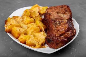 Pork loin steak and potatoes baked with cheese on a white plate