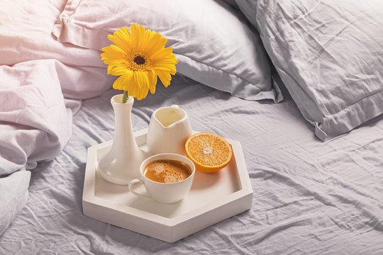 Tray with coffee, milk, orange and yellow flower in a vase.