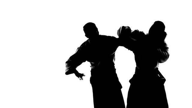 Black silhuettes of two males in keikogi or kimono showing aikido using tanto. Isolated, white. Slow motion. Close up.