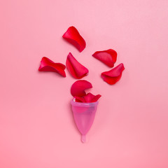 Woman's period concept. Menstrual cup and red rose petals symbolizing blood.