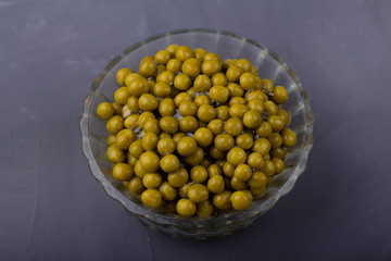 Canned green peas in a glass bowl on a gray background
