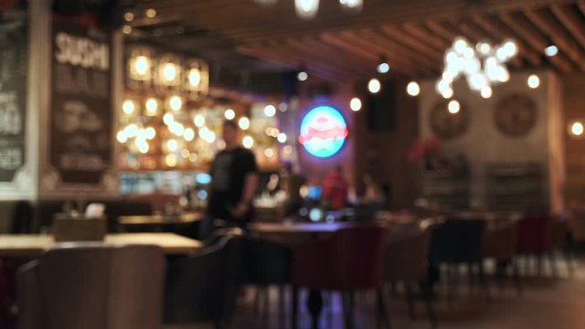 Blurred picture of the interior of a large beautiful restaurant with bright lighting. The waitress comes to the table and gives the visitors a menu and goes for drinks. Lifestyle. Defocused restaurant