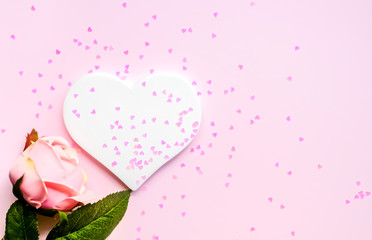 Artificial pink rose and white heart background.