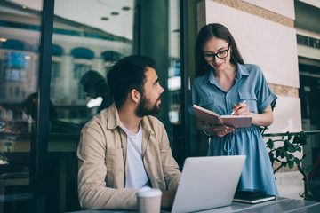Female freelancer making notes near ethnic colleague