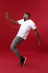 Emotional African-American man listening to music on color background