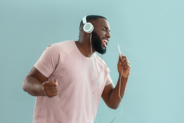 African-American man listening to music and singing on color background - Powered by Adobe
