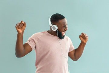 Emotional African-American man listening to music on color background