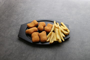 chicken nuggets and french fries  - lunch meal - top view - on a black wooden plate on a dark background 