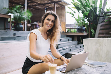 Beautiful happy woman working on laptop and looking at camera