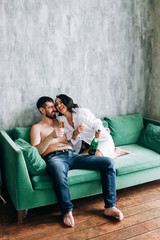 couple celebrating new year, green sofa, laughing, sparkling wine