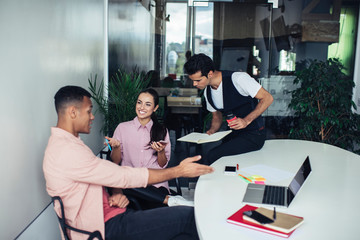 Obraz premium Successful male and female entrepreneurs dressed in casual wear collaborating in office workspace near desktop, smiling colleagues enjoying briefing meeting for training togetherness indoors