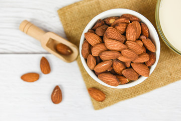 Almond milk in bowl and almonds on wooden scoop on sack