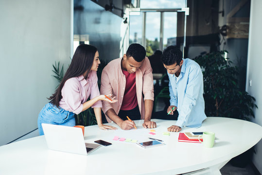 Male and female colleagues collaborating on information making notes during brainstorming at office desktop with netbook, young entrepreneurs concentrated during working process and briefing