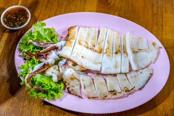Grilled squid with decoration of vegetables in white plate.