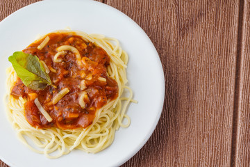 Top view of spagetti bologneese with green basil on white plate over brown background