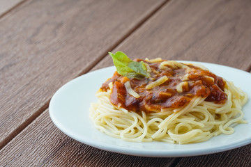 View of spagetti bolognese with green basil on white plate over brown background