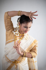 Obraz premium An young and attractive Indian woman in white traditional wear dancing traditional dance form for the celebration of Onam/Pongal in white background. Indian lifestyle.