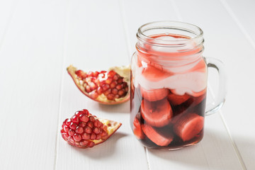 Mug with pomegranate juice and banana slices on a white table.