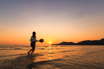 A women hold hat and running on the beach and water splash at sunset.