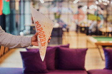 A man holds a paper bag with popcorn on the background of the office, hostel, co-working, restaurant, cinema. A man hands out  popcorn.