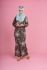 Beautiful female model wearing batik design "baju kurung" with hijab, a modern lifestyle outfit  for Muslim woman isolated over pink background. Eidul fitri fashion and beauty concept.