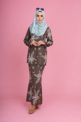 Beautiful female model wearing batik design "baju kurung" with hijab, a modern lifestyle outfit  for woman isolated over pink background. Eidul fitri fashion and beauty concept.