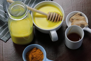 Turmeric latte, golden milk or the anti-inflammatory Indian Haldi Doodh with superfood Turmeric powder, Ginder and Cinnamon sweetened with honey on wooden background