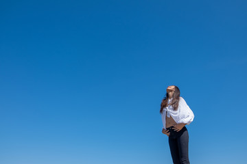 Happy woman with tanned slim body breathing fresh air raising her arms up, enjoying a sunny summer holiday on beach destination against blue sky, outdoors. Travel and well being lifestyle.